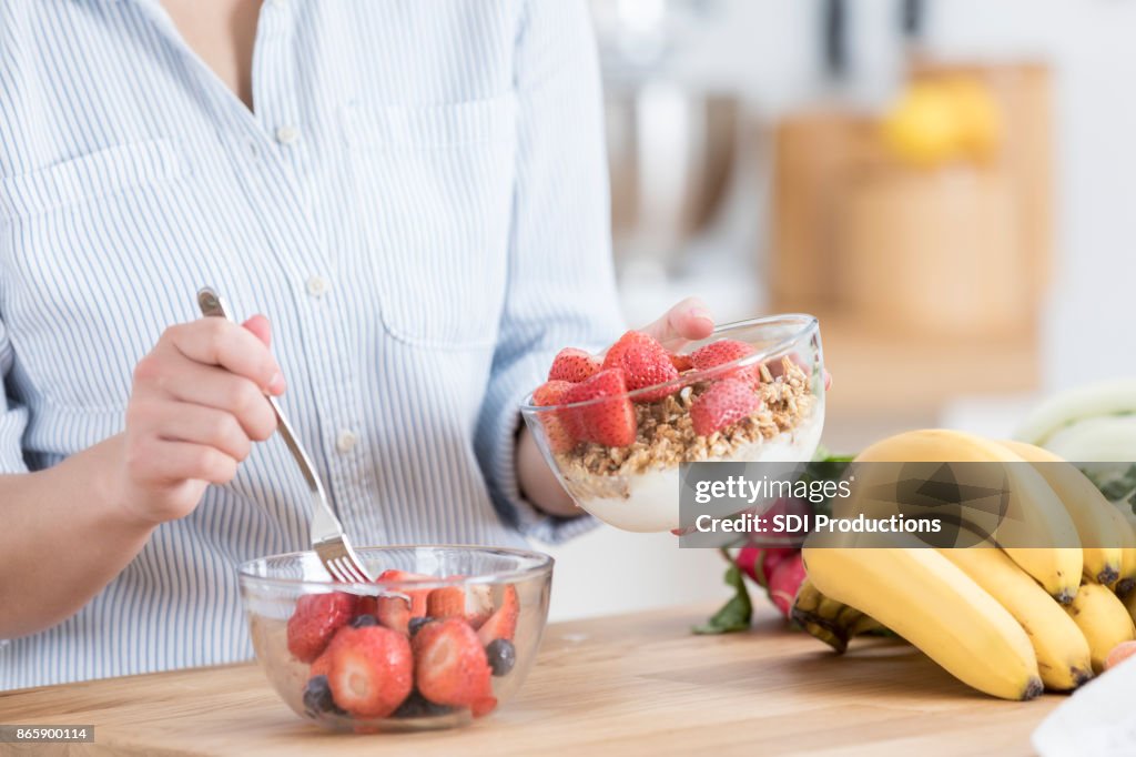 Unrecognizable woman adds strawberries to her parfait