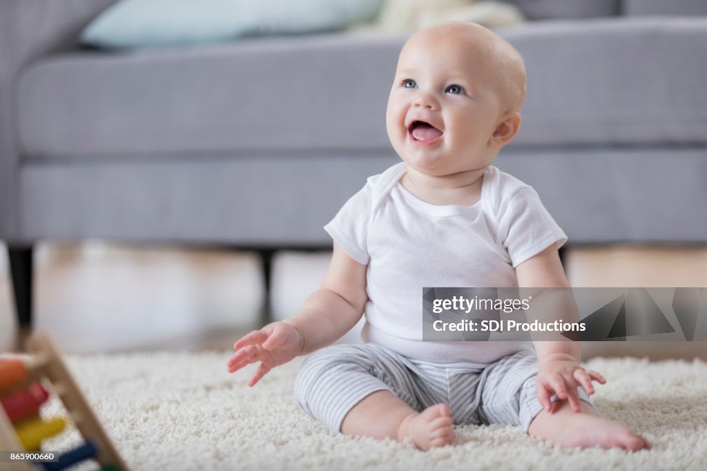 Adorable smiling baby sitting on floor and looking up
