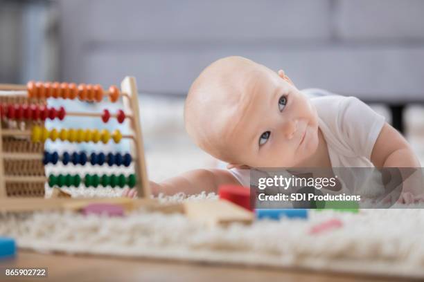 cute baby seeks encouragement as she tries to reach toys - baby girl laying on tummy stock pictures, royalty-free photos & images