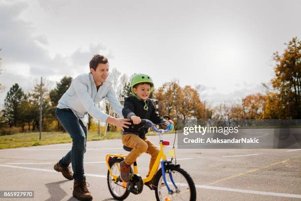 learning to ride a bicycle - father helping son wearing helmet stock pictures, royalty-free photos & images