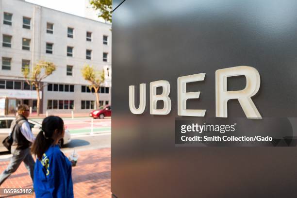 People walk down Market Street past sign with logo at the headquarters of ride-sharing technology company Uber in the South of Market neighborhood of...