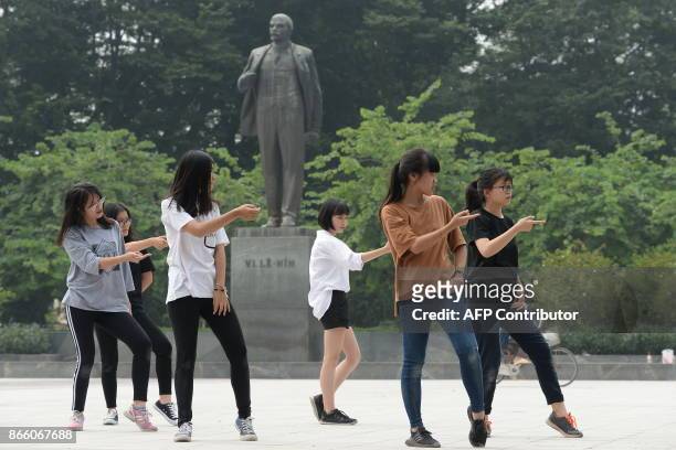 Student girls practice modern dance in front of a statue of Vladimir Lenin, Russian communist leader, at a public park in Hanoi on October 25, 2017....