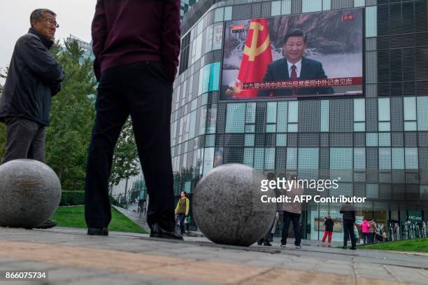 Residents watch a large screen showing Chinese President Xi Jinping attending the Communist Party of China's new Politburo Standing Committee, the...