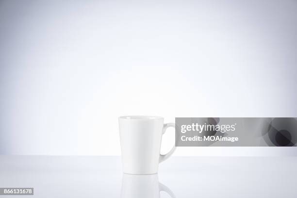 a white porcelain cup on a table indoors - coffee cups table stockfoto's en -beelden