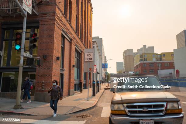 The sun is almost entirely obscured by smoke from the Napa wildfires as a woman wearing a pollution mask walks down Folsom Street in San Francisco,...