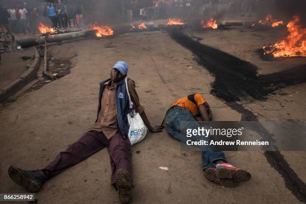 Men lay on the ground in front of a burning roadblock lit in protest for opposition presidential candidate Raila Odinga, in the Kibera slum, on...