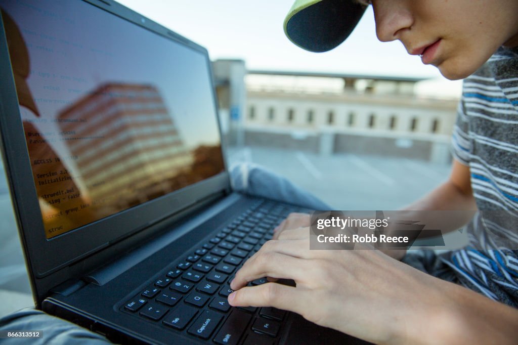 A teenage boy hacking with a laptop computer to commit cyber crime