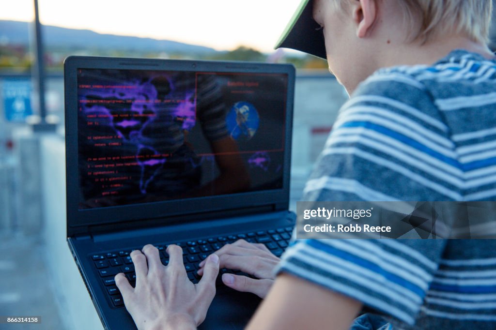 A teenage boy hacking with a laptop computer to commit cyber crime