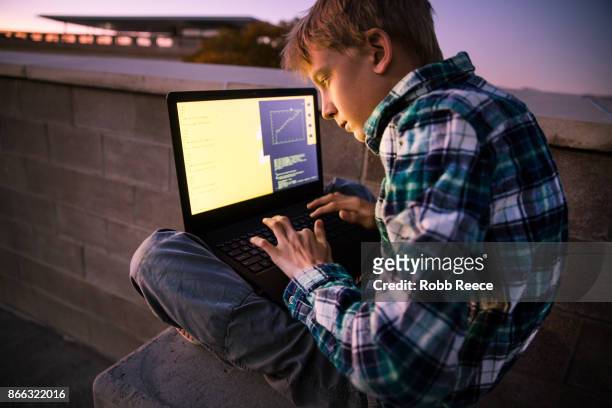 a teenage boy hacking with a laptop computer to commit cyber crime - robb reece stock-fotos und bilder