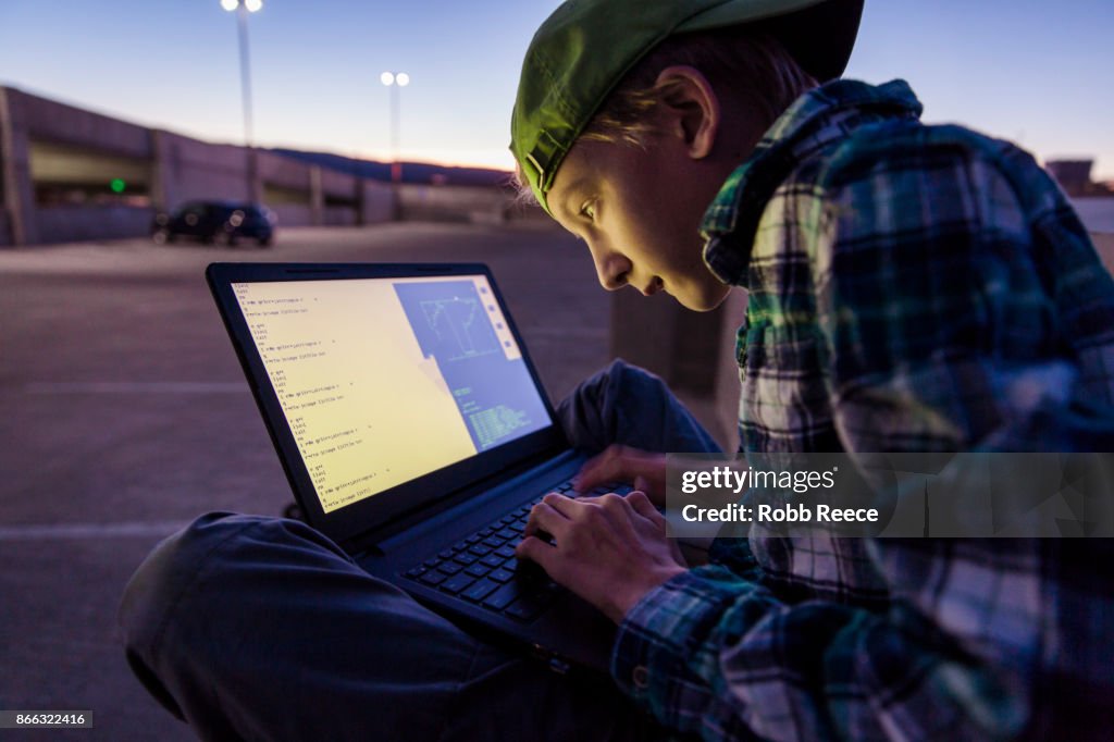 A teenage boy hacking with a laptop computer to commit cyber crime