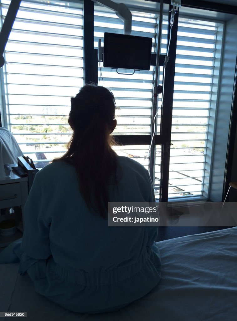 A sick woman at the hospital looks pensive out the window while receiving drip medication