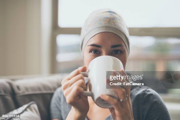 young woman with cancer drinking tea in her living room - fight illness stock pictures, royalty-free photos & images