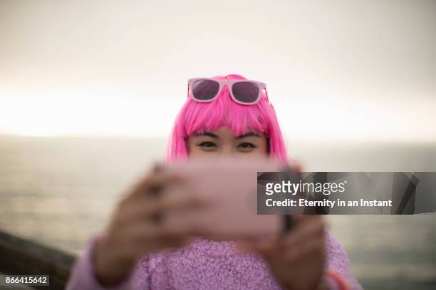 young woman with pink hair taking a photo with her mobile phone - fotografieren stock-fotos und bilder