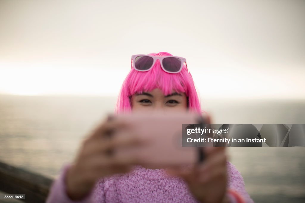 Young woman with pink hair taking a photo with her mobile phone