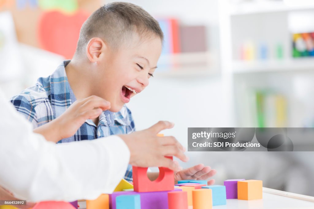 Unrecognizable teacher helps young boy with blocks