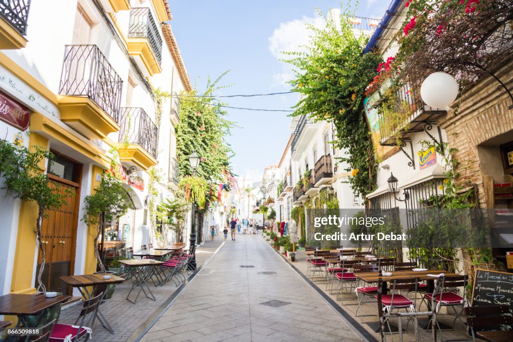 People visiting the beautiful narrow streets in the south of Spain with white houses and vegetation with flowers during trip in the sunny Andalucia.