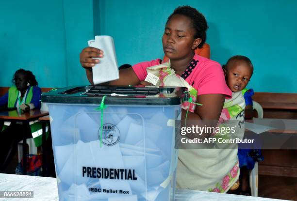 Woman is watched by a young child as she casts her vote into a ballot box at a polling station at Mutomo Primary School in Kiambu on October 26 as...