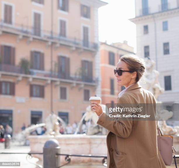 elegant woman walking with takeaway coffee in sustainable coffee cup, piazza navona, rome - green coat foto e immagini stock