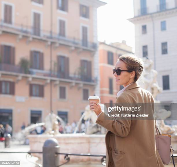 elegant woman walking with takeaway coffee in sustainable coffee cup, piazza navona, rome - holding sunglasses stockfoto's en -beelden