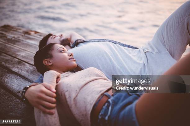 young romantic multi-ethnic couple relaxing together on wooden jetty - couple jetty stock pictures, royalty-free photos & images