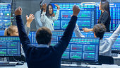 Multi-Ethnic Team of Traders Have Successful Day at the Stock Exchange Office. Dealers and Brokers Buy and Sell Stocks on the Market, they Celebrate Profitable Transaction. Monitors Display Relevant Infographics, Data and Numbers.