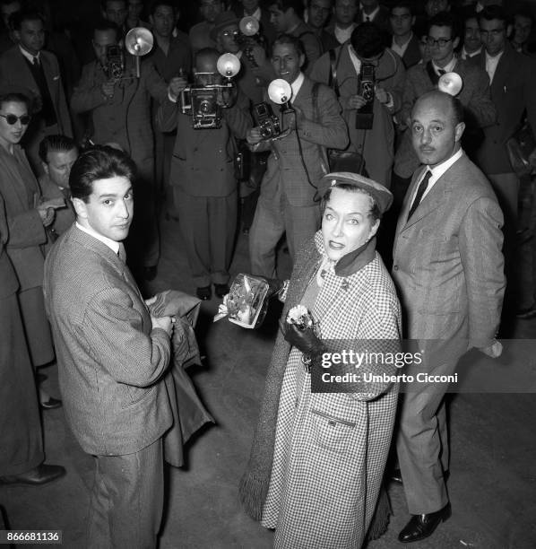 American actress and producer Gloria Swanson photographed in Termini station in Rome in 1955. Many photographers are taking photos of her.