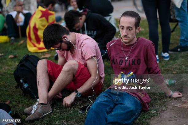 People listen to Catalan Parliament proceedings on the news as Catalan independence supporters gather outside the Parliament of Catalonia on October...