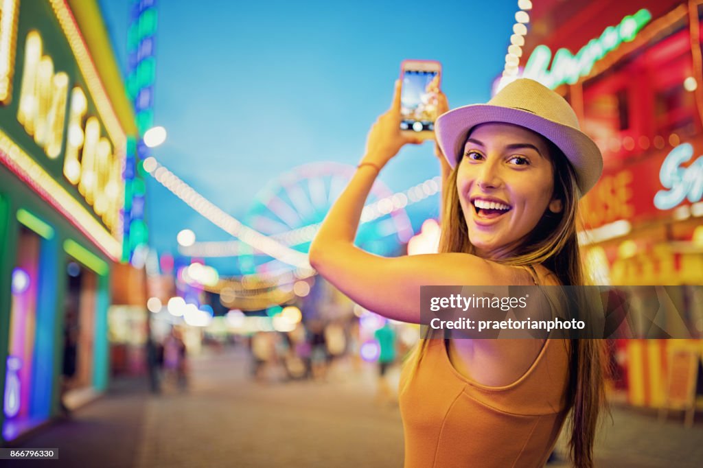 Glückliches Mädchen ist mit ihrem Handy in einen Jahrmarkt fotografieren.