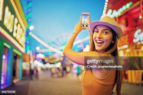 ragazza felice sta scattando foto con il suo cellulare in un funfair - fair game foto e immagini stock