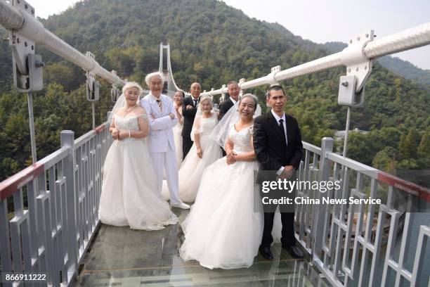 Four couples in wedding dress attire pose for a photo in celebration of their golden wedding anniversary on a transparent glass bridge on October 26,...