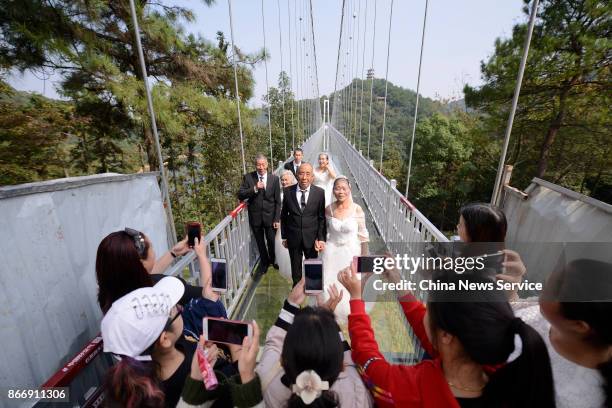 Tourists take photos of four couples in wedding dress attire who pose for a photo in celebration of their golden wedding anniversary on a transparent...