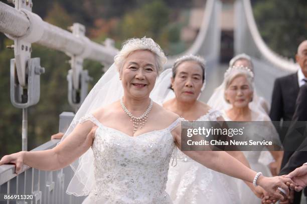 Four couples in wedding dress attire pose for a photo in celebration of their golden wedding anniversary on a transparent glass bridge on October 26,...