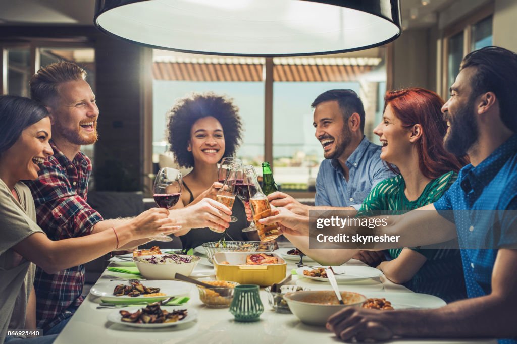 Groep gelukkige vrienden roosteren tijdens het eten bij de eettafel.