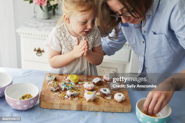 woman and child decorating doughnuts together - kuchen dekorieren stock-fotos und bilder