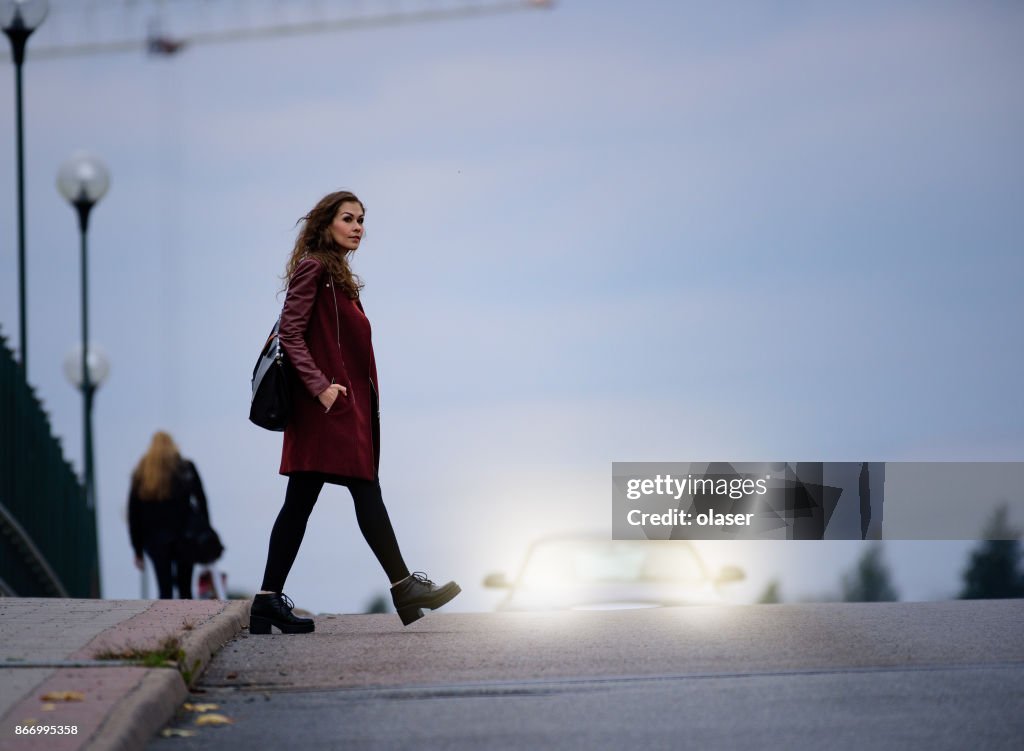Donna attraversa strada ponte buio, auto sullo sfondo
