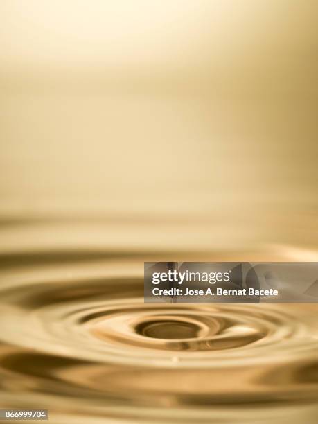 group of drops on line suspended in the air, falling down on a water surface that forms figures and abstract forms, on a gold-colored background - sine wave fotografías e imágenes de stock