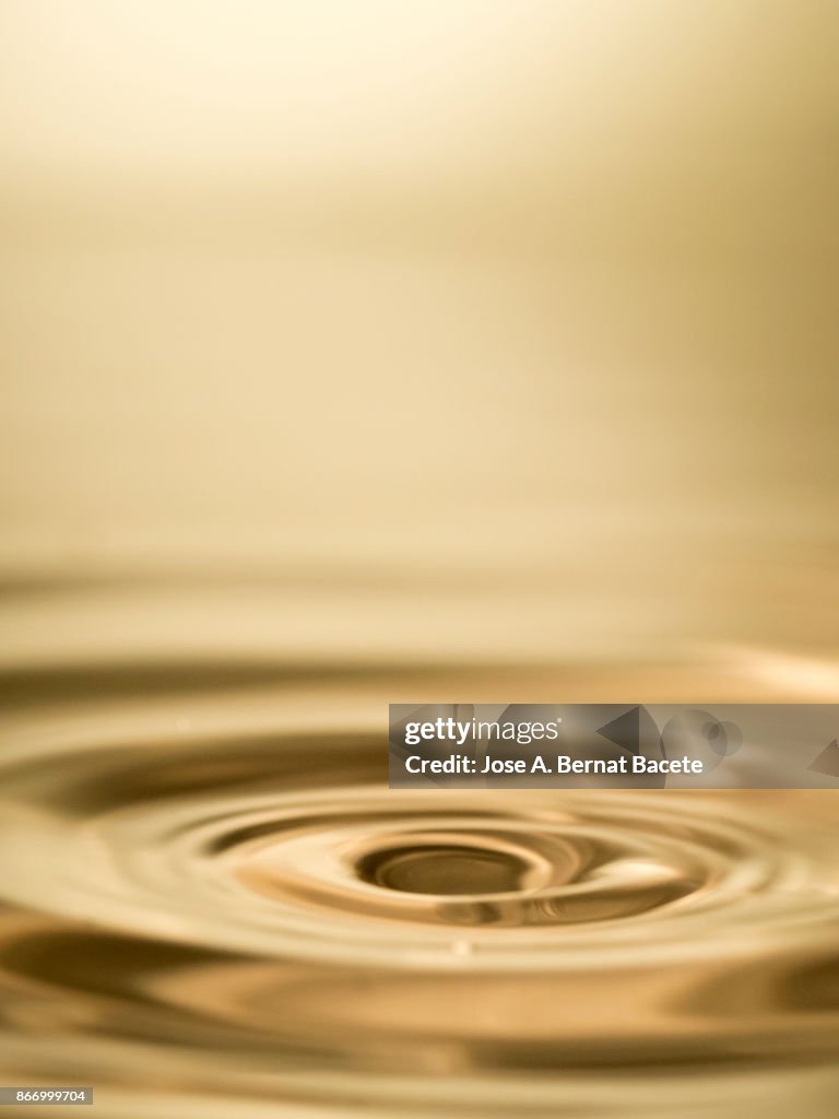 Group of drops on line suspended in the air, falling down on a water surface that forms figures and abstract forms, on a gold-colored background