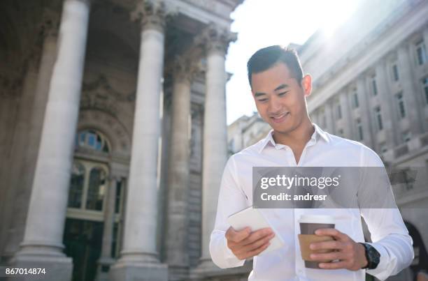 asian business man texting on his cell phone and having coffee to go - man atm smile stock pictures, royalty-free photos & images