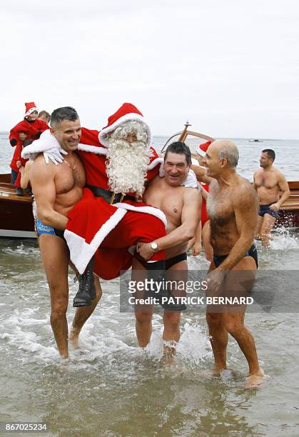 Un homme déguisé en père Noël est porté par les nageurs du traditionel bain de Noël à son arrivée sur la plage d'Arcachon, le 17 décembre 2005, où il...