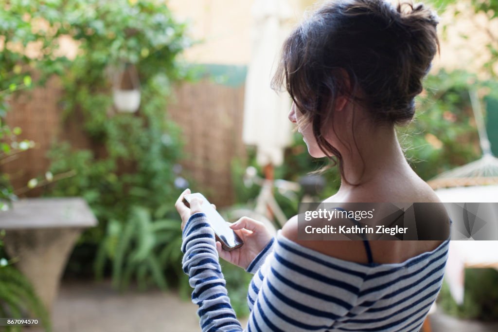 Woman standing in backyard, using smartphone