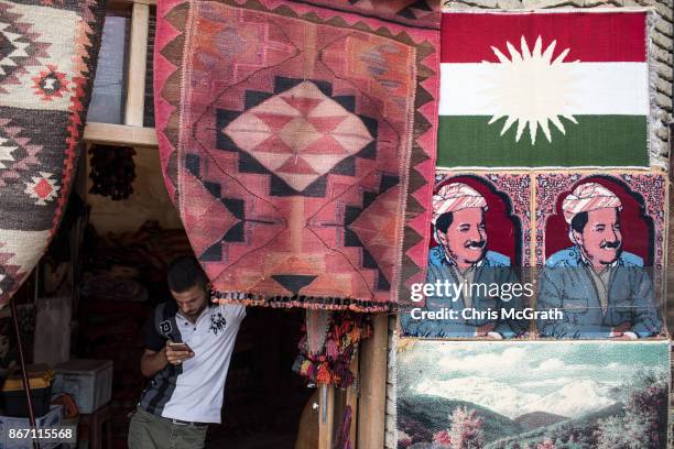 Man checks his phone at a rug store next to a portrait of Kurdistan President Massud Barzani in the old city on October 27, 2017 in Erbil, Iraq....