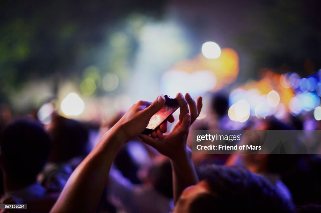 Hands holding smartphone reach up to take picture of fireworks show
