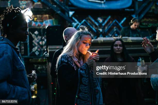 young partygoer lighting a joint while dancing with friends - cannabis drugs stockfoto's en -beelden