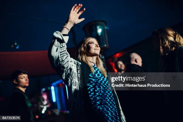 young woman holding hand in the air while dancing at nightclub - 30 40 woman stock-fotos und bilder