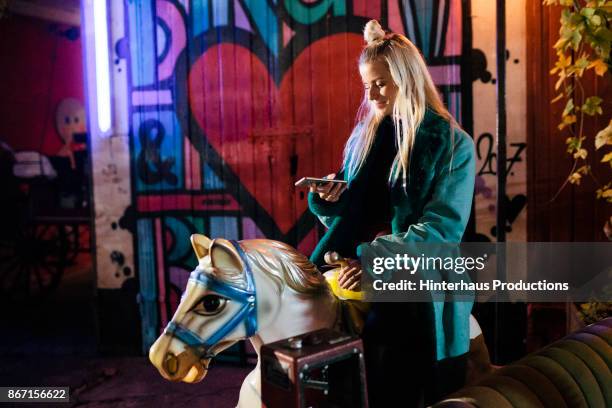 stylish young partygoer riding on a mechanical horse at open air nightclub - night out stock-fotos und bilder