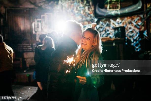 girl laughing with boyfriend while holding sparkler at open air nightclub - couple night stock-fotos und bilder