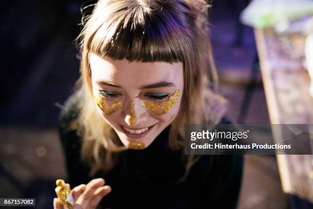 girl painting her face with gold glitter while out clubbing - dunkelheit spass stock-fotos und bilder