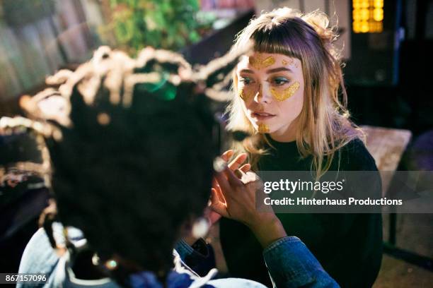 girl painting her friends face with gold glitter while out clubbing together - face paint stock-fotos und bilder