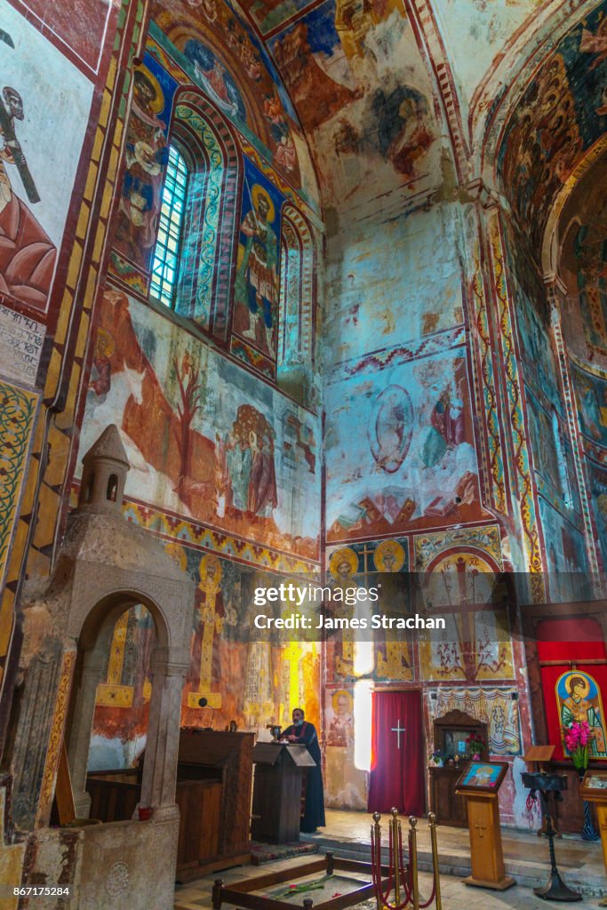 Colourful frescoes painted between 12th and 18th centuries on walls of Cathedral of the Virgin, Gelati Monastery (UNESCO World Heritage Site), loom above priest in foreground, Kutaisi, Georgia