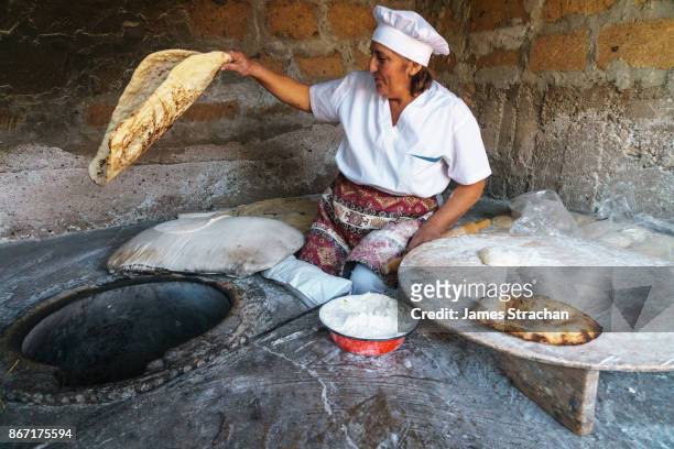 traditional breadmaker pulling fresh lavash bread out of her clay oven, (smaller bread is bokon), yerevan, armenia (model release) - armenia ストックフォトと画像